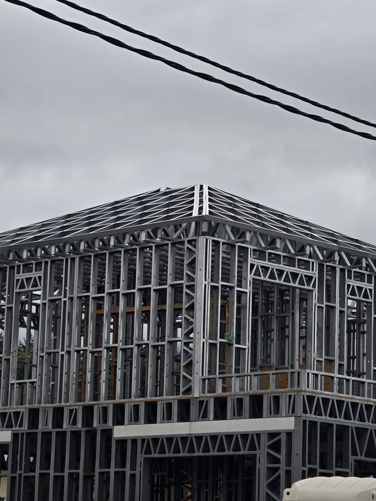 Vista exterior de la estructura completa de acero ligero (Steel Frame) de una vivienda de dos plantas con el esqueleto del tejado a cuatro aguas montado, bajo un cielo nublado.